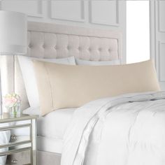 a bed with white sheets and pillows in a bedroom next to a lamp on a night stand