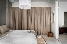 a white bed sitting under a light fixture in a bedroom next to a window with drapes