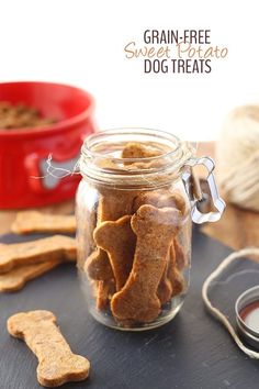 a glass jar filled with dog treats next to a red bowl full of dog biscuits