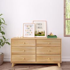 a wooden dresser with two pictures on top and a potted plant in the corner