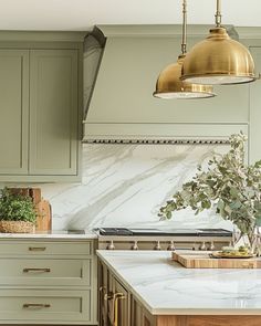 a kitchen with green cabinets and marble counter tops, gold pendant lights over the stove