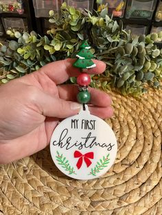 a hand holding a christmas ornament with the words my first christmas on it