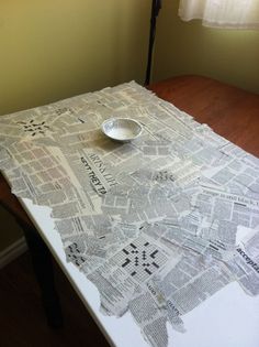 a bowl sitting on top of a table covered in newspaper paper next to a lamp