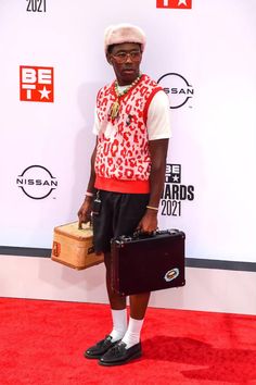 a man with a suit case and hat on the red carpet at an awards event