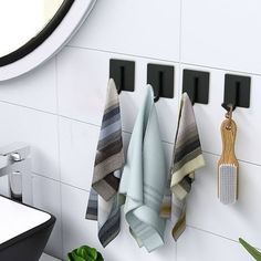 three towels hanging on the wall next to a potted plant and sink in a white tiled bathroom