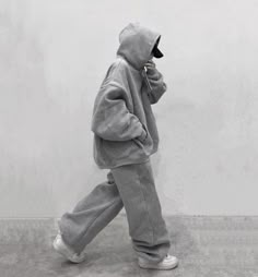 a person in a grey hoodie and sweatpants walks while talking on a cell phone