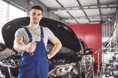 a man standing in front of a car holding a wrench and giving the thumbs up