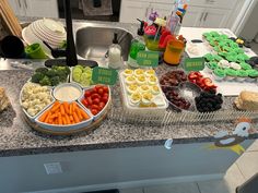 a kitchen counter topped with lots of trays filled with fruit and veggies