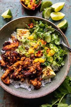 a bowl filled with chicken and rice next to lime wedges on a table top