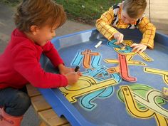 two children playing with letters and numbers on a play table