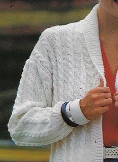 a woman wearing a white cardigan and holding her hand up to her chest while talking on a cell phone