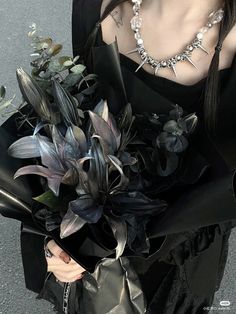 a woman wearing a black dress holding a bouquet of flowers and necklaces on her neck