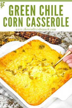 green chile corn casserole in a white baking dish with a hand holding a wooden spoon