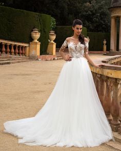 a woman standing next to a stone wall wearing a white dress with lace on it