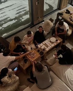 a group of people sitting around a table with pizzas on it in front of large windows