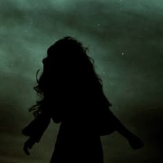 the silhouette of a woman with long hair against a dark sky, holding her arms out