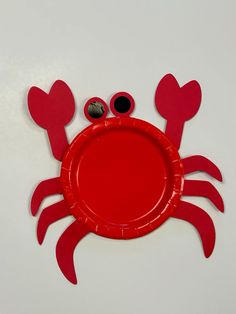 a red paper plate with two eyes and a crab design on it, sitting on a white surface