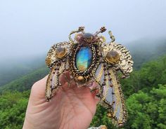 a hand holding a brooch with a blue and yellow insect on it's back