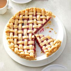 a pie on a white plate with one slice cut out and two cups of tea in the background