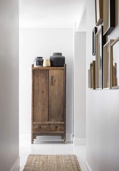 a wooden cabinet sitting on top of a white floor next to a wall filled with pictures