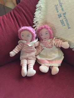 two dolls sitting next to each other on a red couch with a white pillow behind them