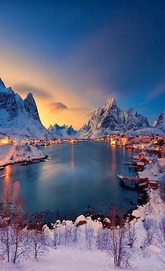 the mountains are covered in snow and lit up by lights at night, with boats on the water