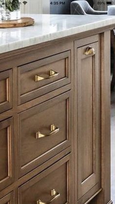 a kitchen island with marble top and brass pulls on the drawers in front of it