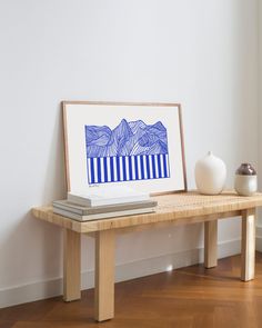 a wooden table topped with a white vase next to a painting on top of it