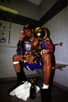 a man sitting on a toilet talking on a cell phone while holding a trophy in his hand