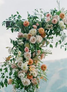 an arrangement of flowers hanging from the side of a wooden structure with greenery and foliage