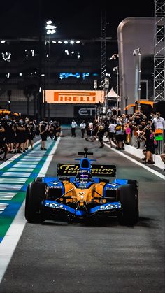 a blue and yellow racing car driving down a race track with people watching from the sidelines