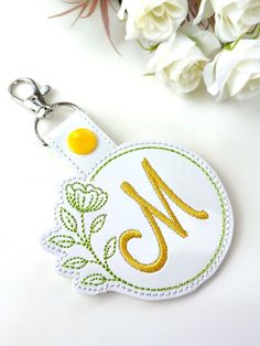 a keychain with the letter m on it and flowers in the back ground