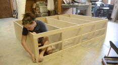 a woman kneeling down in front of a bed frame that is made out of plywood