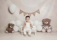 a baby sitting on a bench in front of balloons and teddy bears