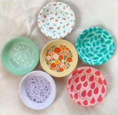 four bowls with different designs on them sitting next to each other in the middle of a white sheet