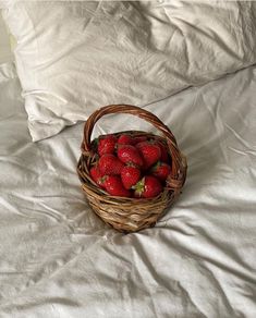 a wicker basket filled with strawberries on top of a white sheet covered bed