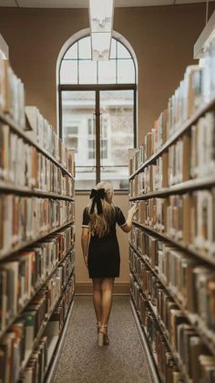 a woman is walking through a library with lots of books on the shelves and she has her back to the camera