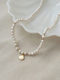 This genuine baroque Pearl necklace is the perfect accessory to elevate your summer look! This stunning necklace is crafted with off round irregular pearls and features a beautiful 14K Gold Filled or 925 Silver scallop shell charm. It's the perfect addition to your jewelry collection and is sure to become a beachy ocean inspired wardrobe staple.  * 14K Gold Filled or 925 Sterling Silver accents * Adjustable 18" - 20" length * 10mm 14K Gold Filled or 925 Sterling Silver Scallop Shell charm * Natu Shell-shaped Pearl Necklace With Pearl Pendant, Shell-shaped Pearl Charm Necklaces, Elegant Pearl Necklace With Shell Shape, Shell-shaped Pearl Drop Necklace, Pearl Drop Shell Pearl Necklace, Elegant Shell-shaped Pearl Chain Necklace, Elegant Gold Shell Necklace With Round Beads, Beaded Necklace With Baroque Pearl And Pearl Charm, Beaded Necklace With Baroque Pearl Charm