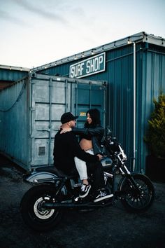 a man and woman sitting on a motorcycle in front of a shipping container at the same time