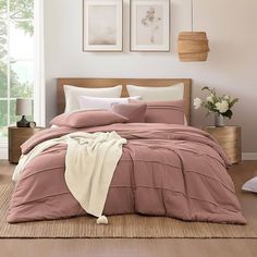 a bed with pink comforter and pillows in a room next to two pictures on the wall