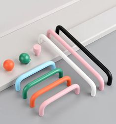 four different colored handles are on the floor next to an orange ball and two green balls