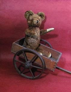 a brown teddy bear sitting in a wooden wagon