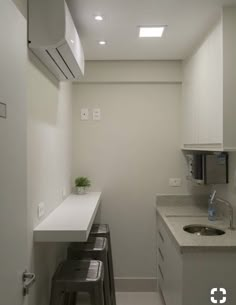 an empty kitchen with white cabinets and counter tops, two stools are in front of the sink