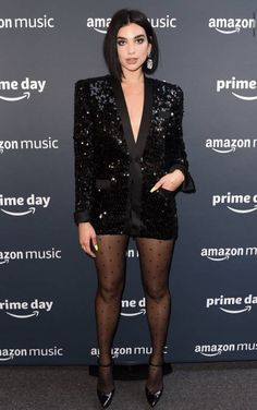 a woman standing in front of an amazon music sign wearing black tights and a sequin blazer