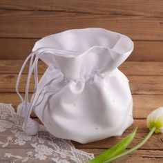 a small white bag sitting on top of a wooden table next to a tulip