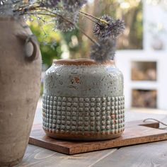 a ceramic vase sitting on top of a wooden table next to a potted plant