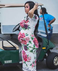 a woman in a floral dress is standing next to a golf cart and holding her arm up