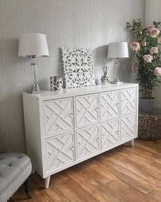 a white dresser sitting on top of a hard wood floor next to a vase filled with flowers