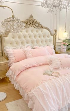 a bed with pink comforter and pillows in a white room next to a chandelier