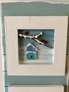 a white frame with a blue birdhouse and tree branch in it